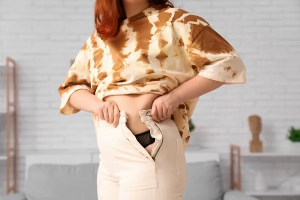 Image of woman trying to do her trousers up after pregnancy weight gain Dysart